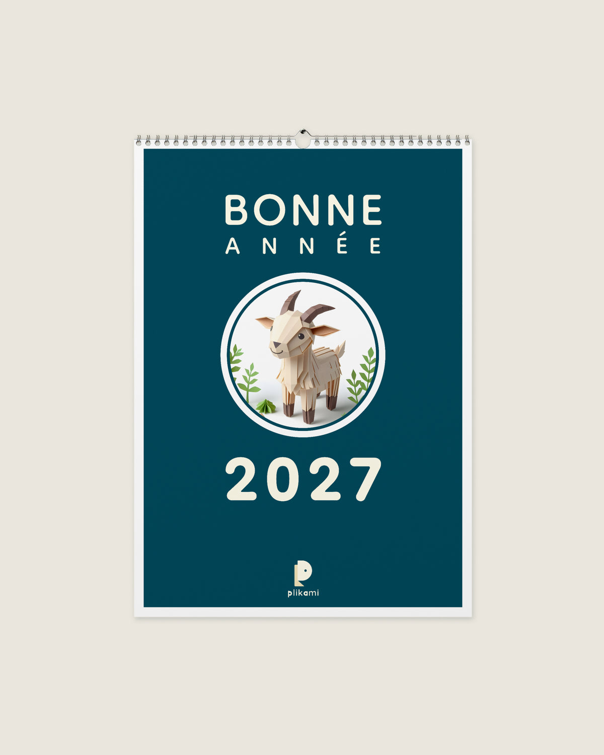 Calendrier mural à reliure spirale, couverture sarcelle portant le titre Bonne Année 2027 et une chèvre en papier plié dans un médaillon rond.