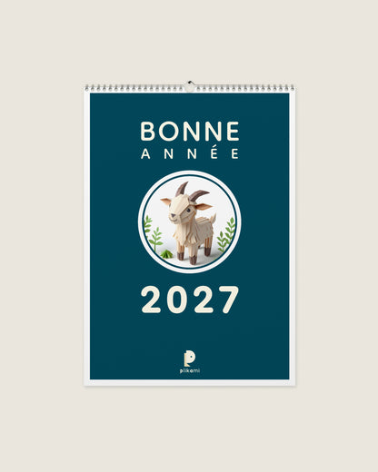 Calendrier mural à reliure spirale, couverture sarcelle portant le titre Bonne Année 2027 et une chèvre en papier plié dans un médaillon rond.