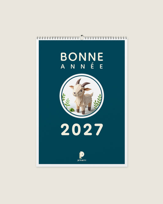 Calendrier mural à reliure spirale, couverture sarcelle portant le titre Bonne Année 2027 et une chèvre en papier plié dans un médaillon rond.
