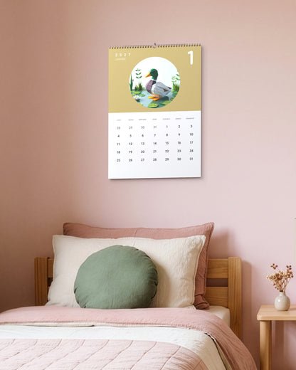 Calendrier accroché au mur rose d'une chambre d'enfant, au-dessus d'un lit en bois, ouvert sur janvier : un canard en papier plié sur fond moutarde.