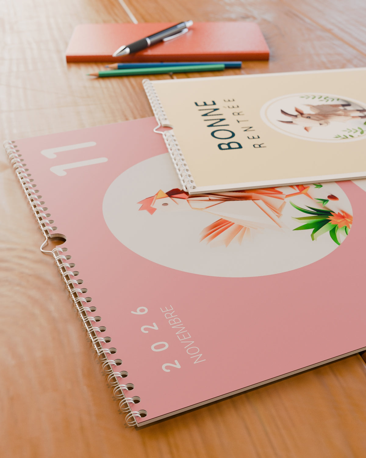 Gros plan sur la reliure spirale et le grain du papier du calendrier mural Bonne Rentrée 2026 / 2027, posé sur un bureau en bois.
