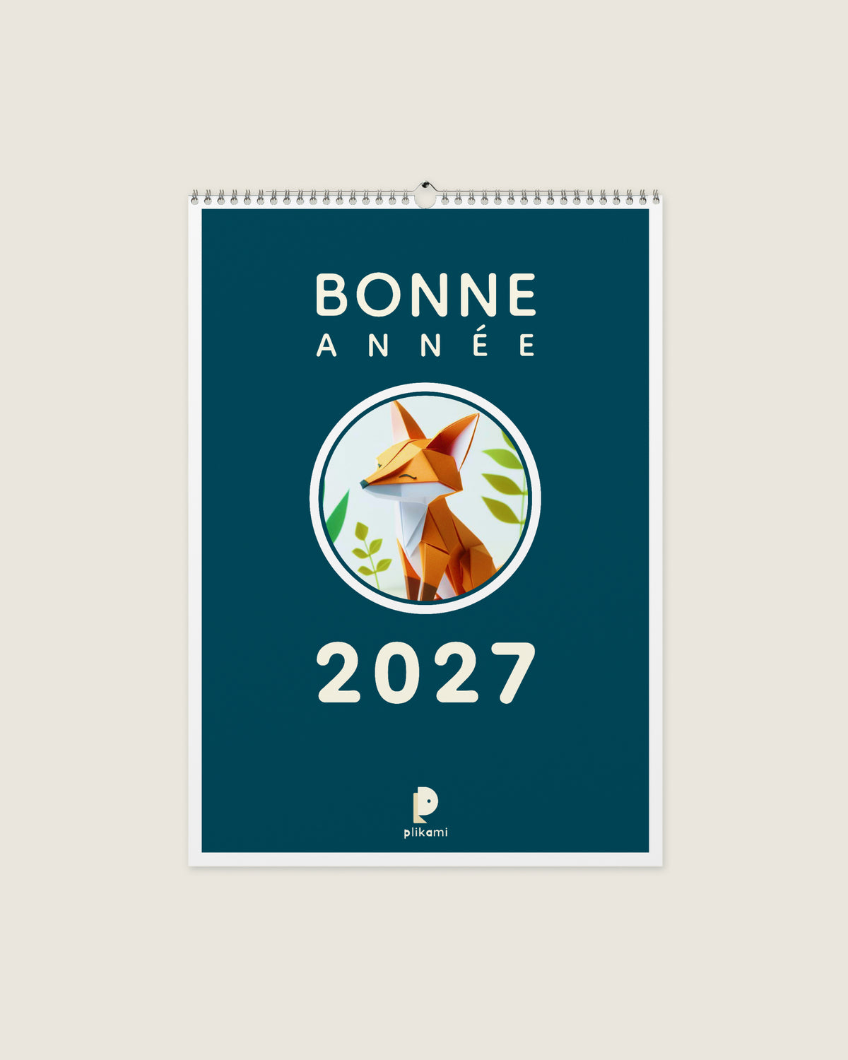 Calendrier mural à reliure spirale, couverture bleu canard portant le titre Bonne Année 2027 et un renard en papier plié dans un médaillon rond.