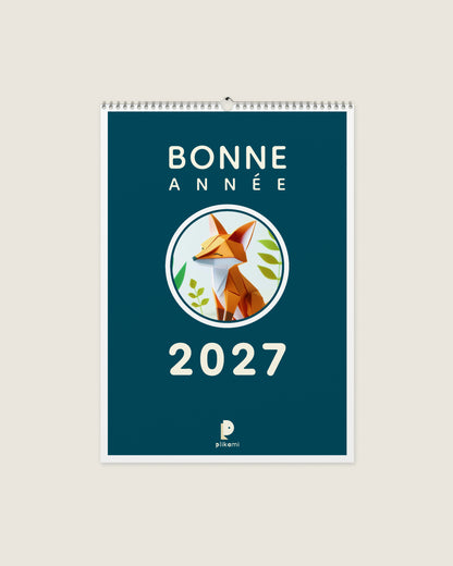 Calendrier mural à reliure spirale, couverture bleu canard portant le titre Bonne Année 2027 et un renard en papier plié dans un médaillon rond.