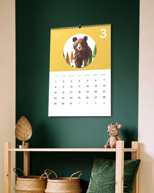 Calendrier accroché au mur vert sapin au-dessus d'une étagère basse en bois avec paniers tressés et peluche, ouvert sur mars : un ours en papier plié sur fond jaune.