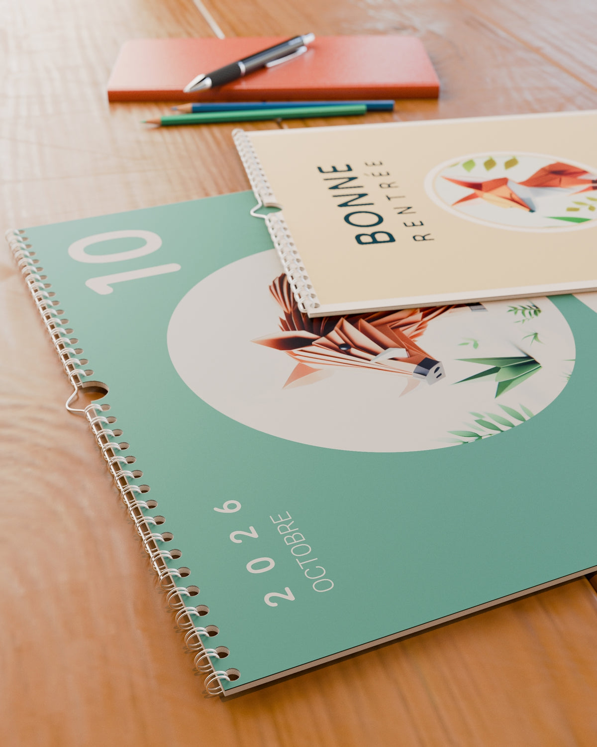 Gros plan sur la reliure spirale et le grain du papier du calendrier mural Bonne Rentrée 2026 / 2027, posé sur un bureau en bois.