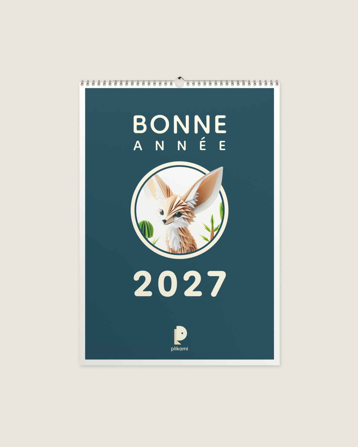 Calendrier mural à reliure spirale, couverture sarcelle portant le titre Bonne Année 2027 et un fennec en papier plié dans un médaillon rond.