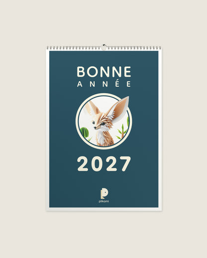 Calendrier mural à reliure spirale, couverture sarcelle portant le titre Bonne Année 2027 et un fennec en papier plié dans un médaillon rond.