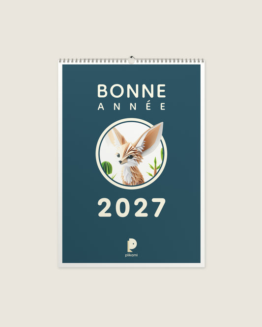 Calendrier mural à reliure spirale, couverture sarcelle portant le titre Bonne Année 2027 et un fennec en papier plié dans un médaillon rond.