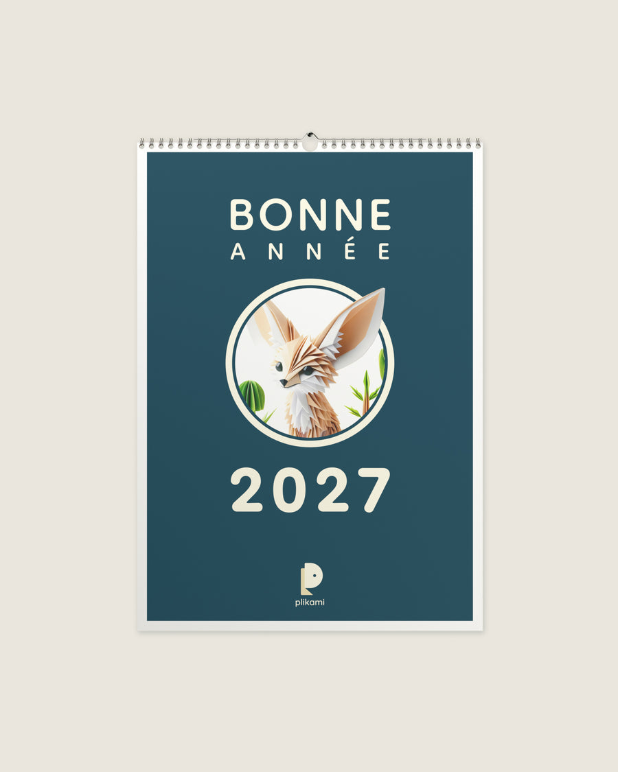 Calendrier mural à reliure spirale, couverture sarcelle portant le titre Bonne Année 2027 et un fennec en papier plié dans un médaillon rond.
