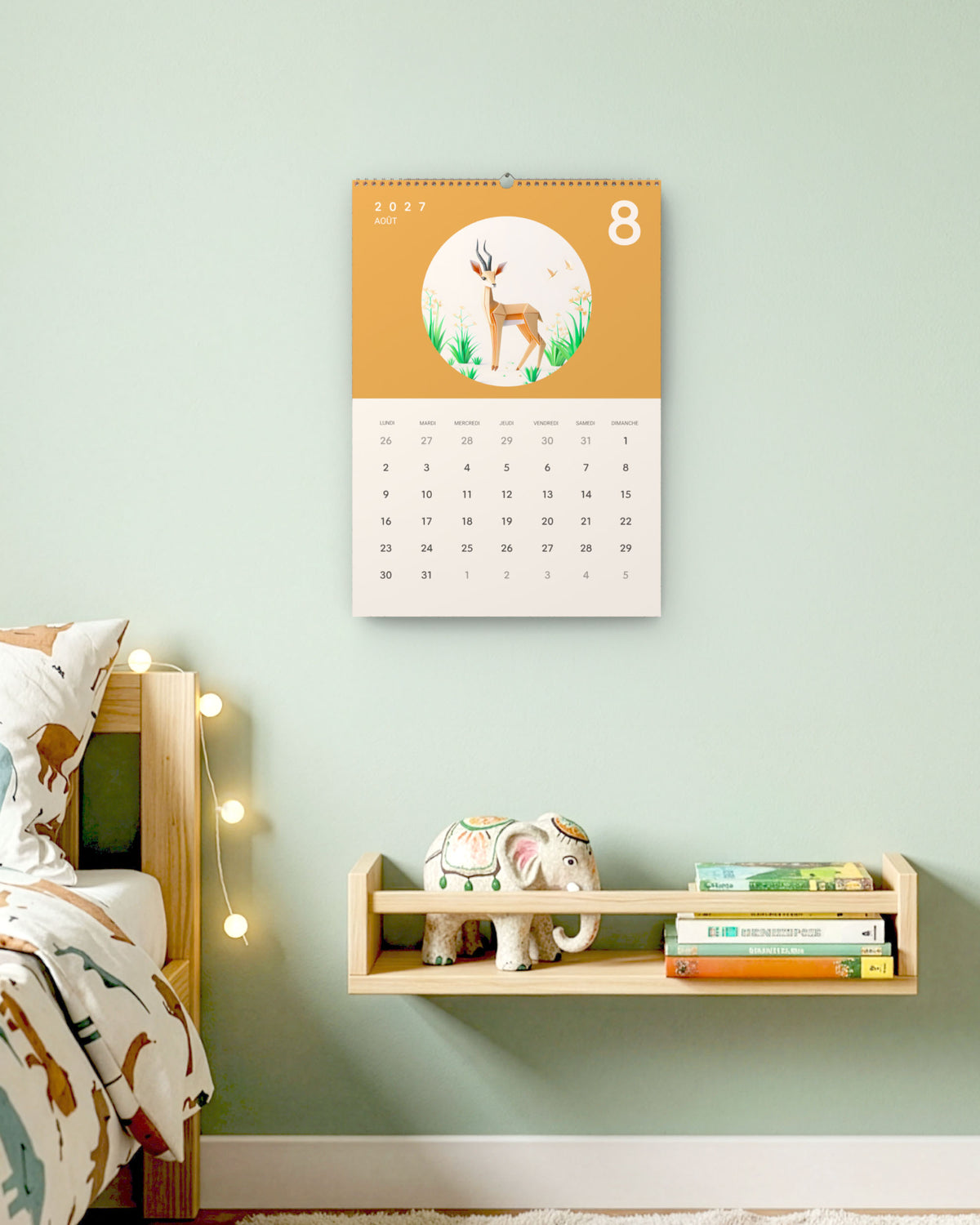 Calendrier accroché au mur vert d'eau d'une chambre d'enfant, au-dessus d'une étagère à livres, ouvert sur août : une gazelle en papier plié sur fond ocre.