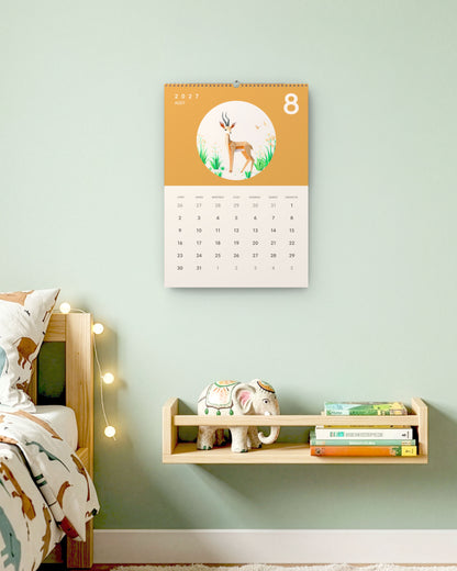 Calendrier accroché au mur vert d'eau d'une chambre d'enfant, au-dessus d'une étagère à livres, ouvert sur août : une gazelle en papier plié sur fond ocre.